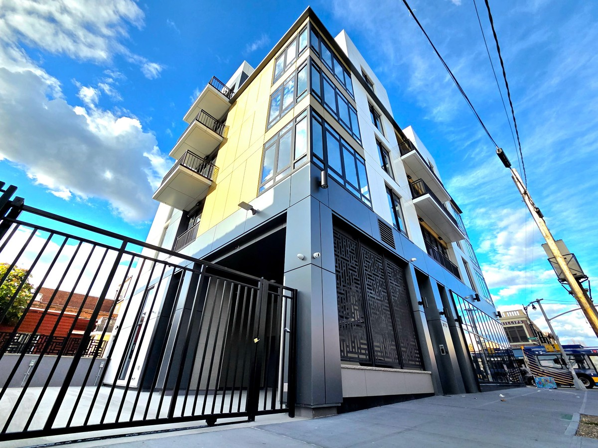 Full low-angle photograph of the 37-18 Astoria building with white, yellow and gray panels, balconies and corner windows